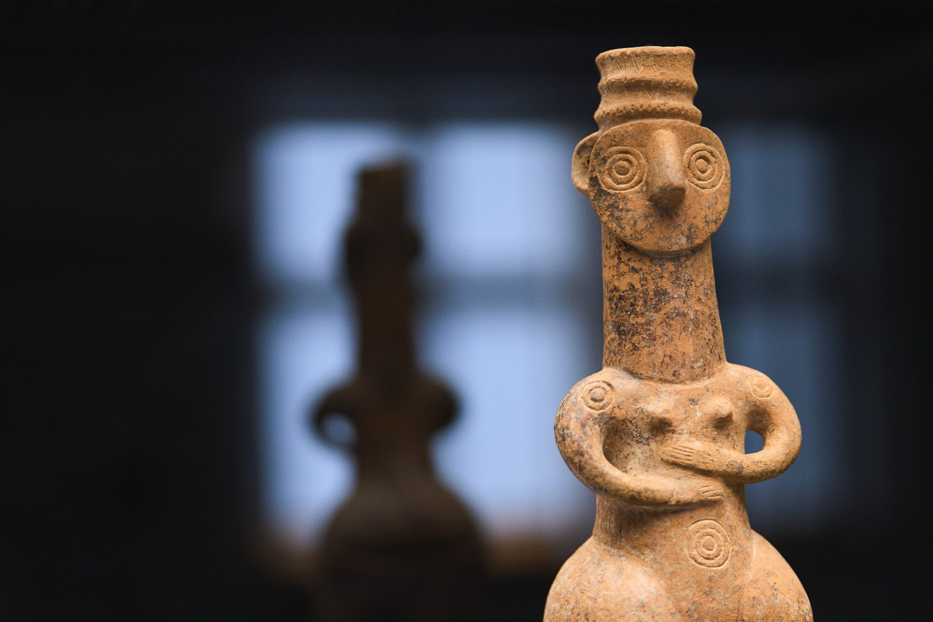 Antike Terrakottafigur, stilisierte menschliche Form mit kunstvoll verzierter Kleidung und runden Gesichtszügen.