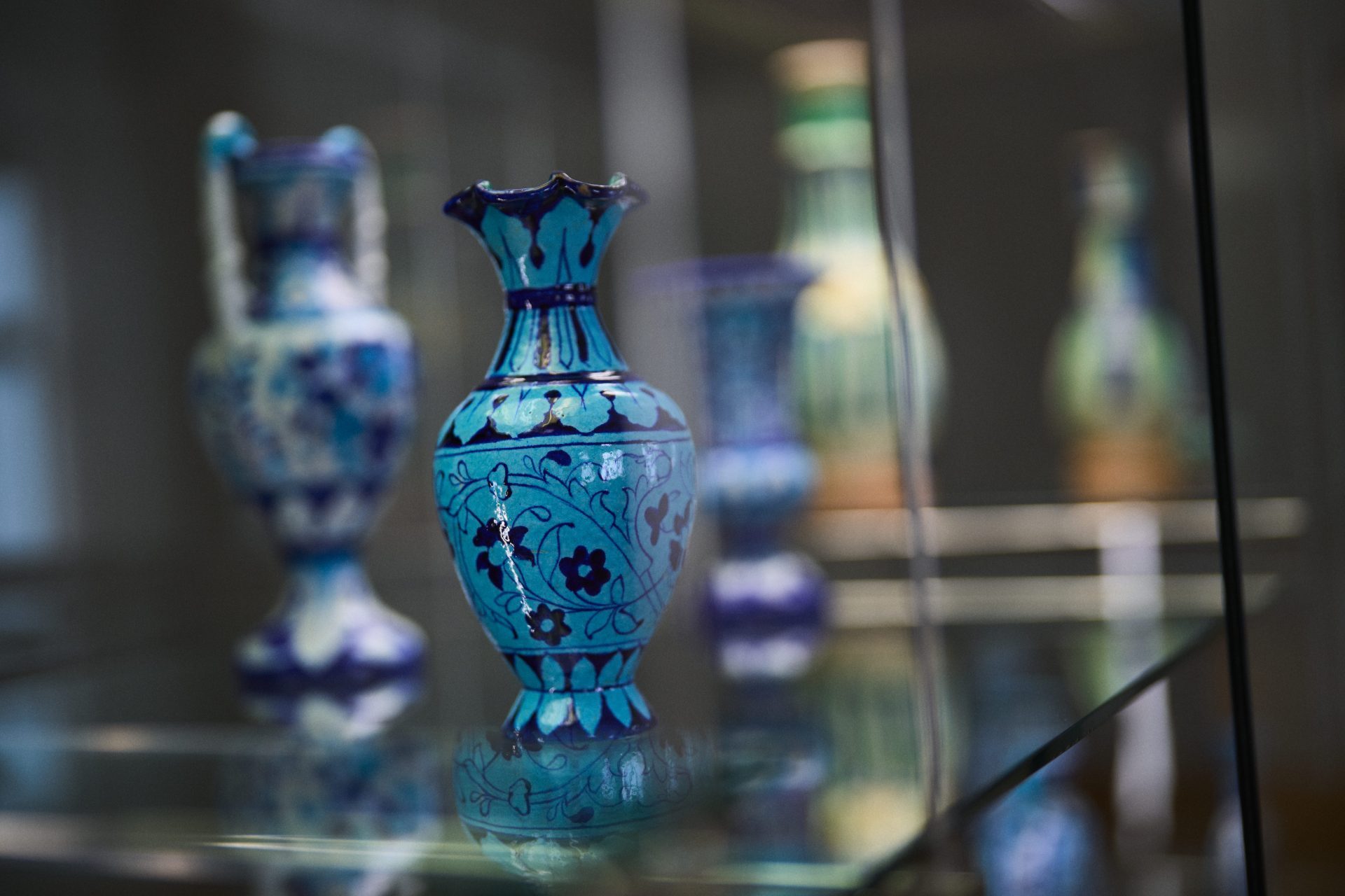Bunte, kunstvoll verzierte Vasen in einer Vitrine, floral gestaltet und in blauen Farbtönen gehalten.