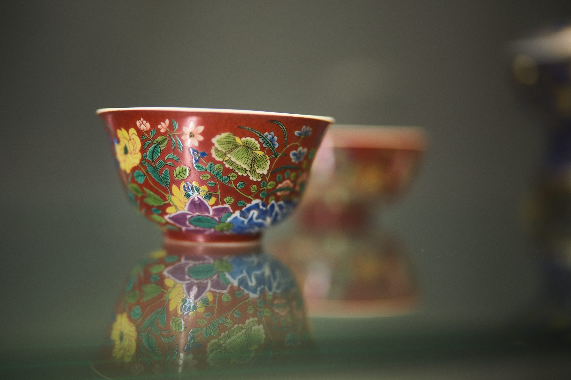 Bunte Schale mit floralen Mustern spiegelt sich auf einer Glasoberfläche, im Hintergrund eine weitere Schale sichtbar.