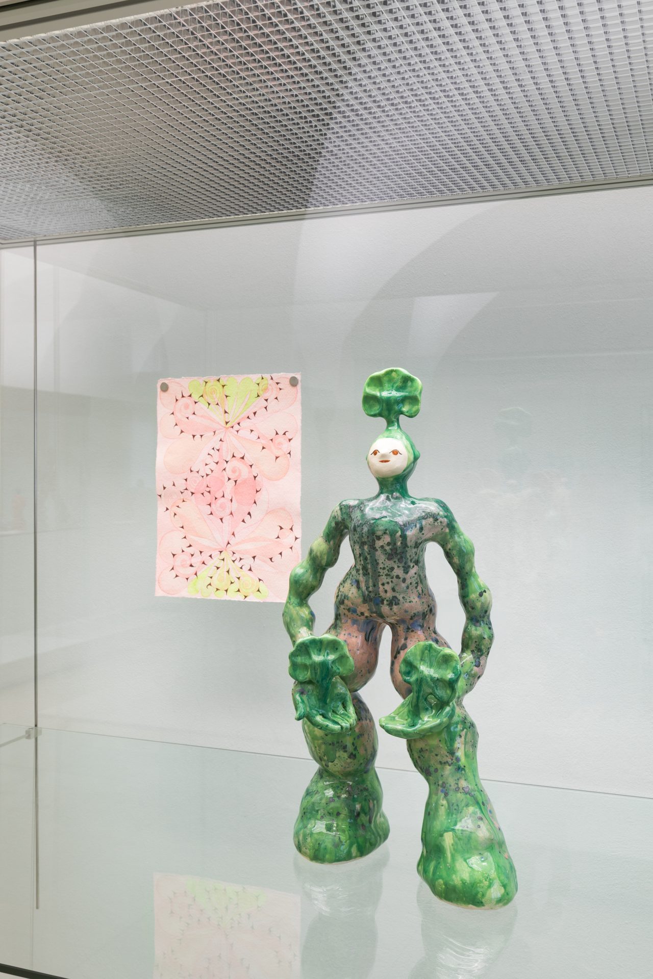Grüne Skulptur in menschlicher Form mit Blattmotiven, neben einem bunten, pinken Kunstwerk.