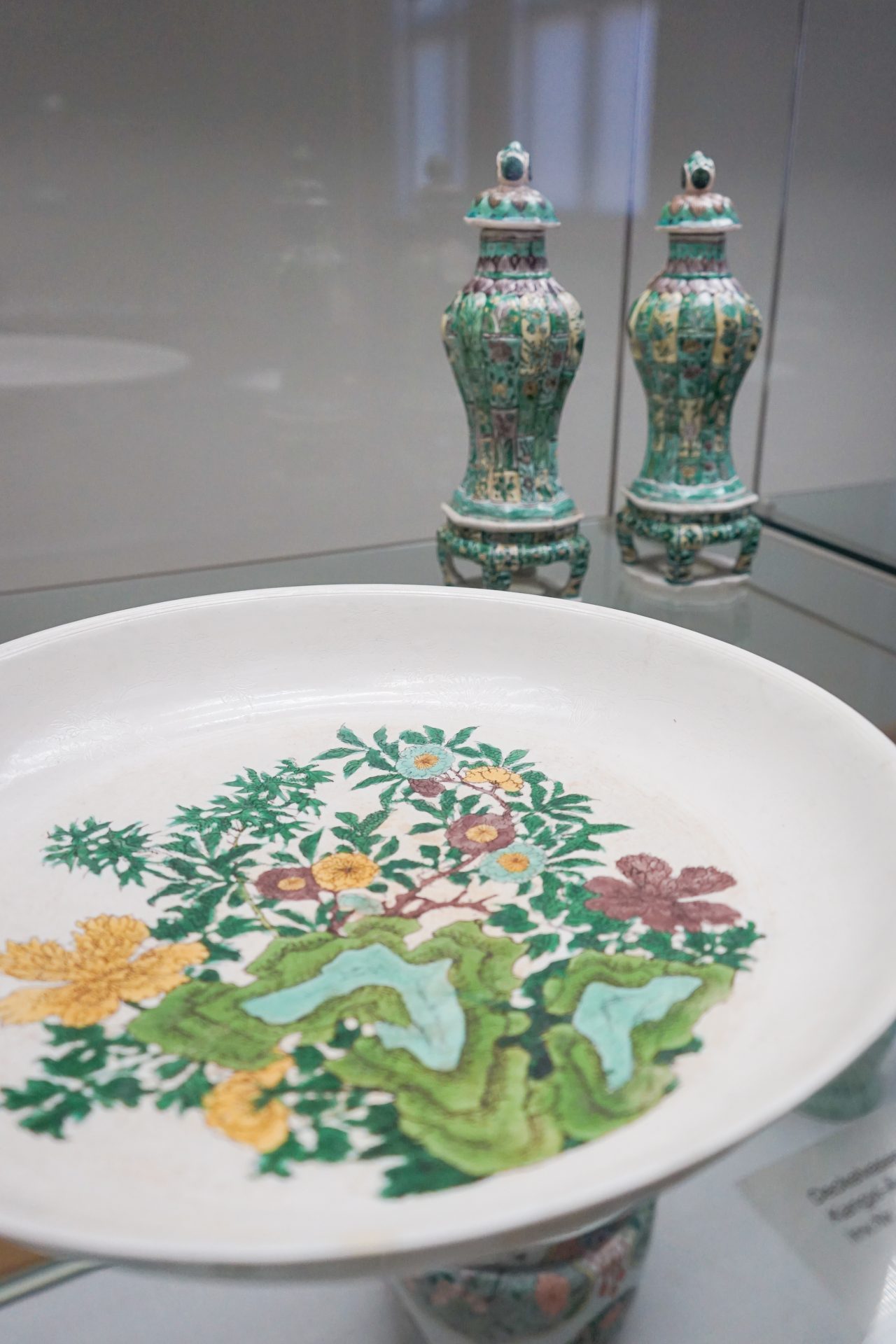 Dekorative Schale mit buntem Pflanzenmuster, im Hintergrund zwei filigrane, verzierte Vasen.