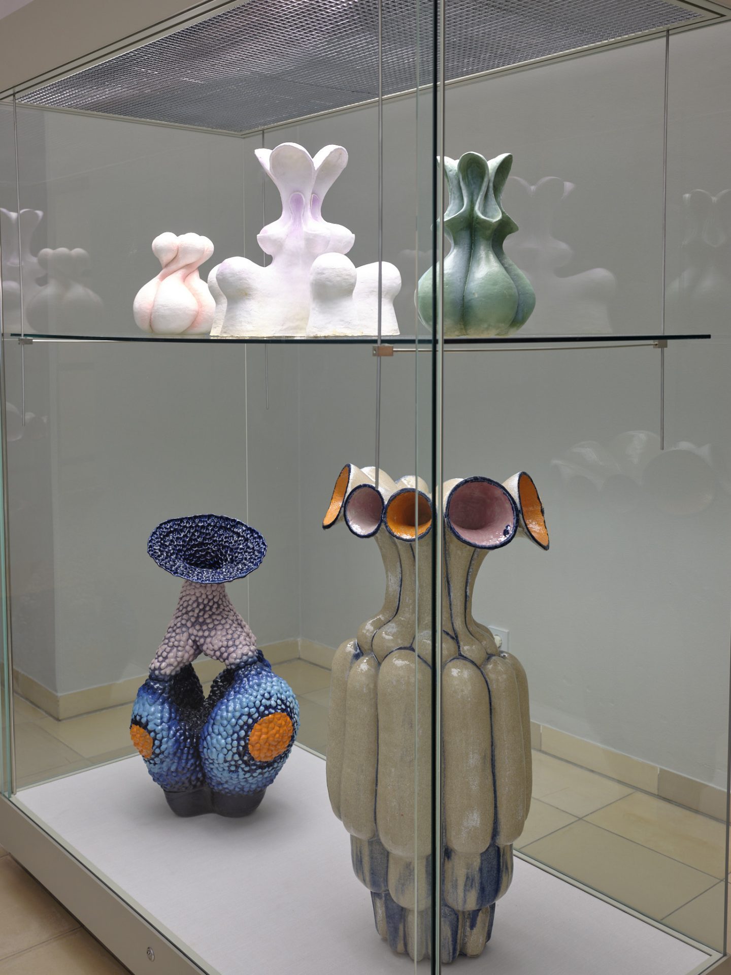 Moderne Kunstwerke in einer Vitrine: bunte Skulpturen mit organischen Formen und verschiedenen Texturen.