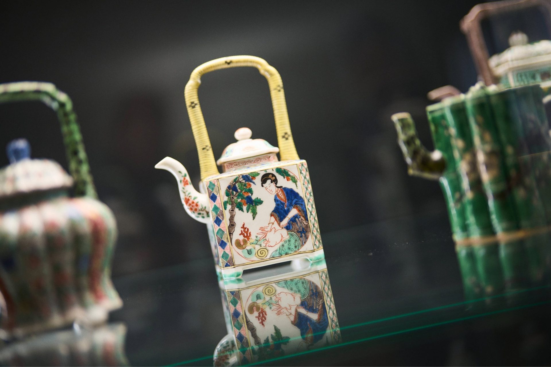 Bunte Teekanne mit quadratischem Design und kunstvollen Motiven auf spiegelnder Oberfläche.