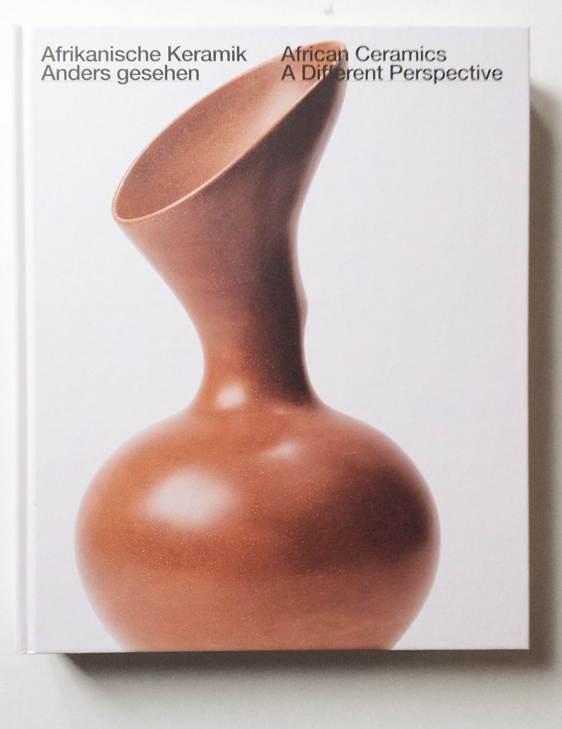 Buchcover über afrikanische Keramik mit stilisiertem, braunem Gefäß und zweisprachigem Titel.