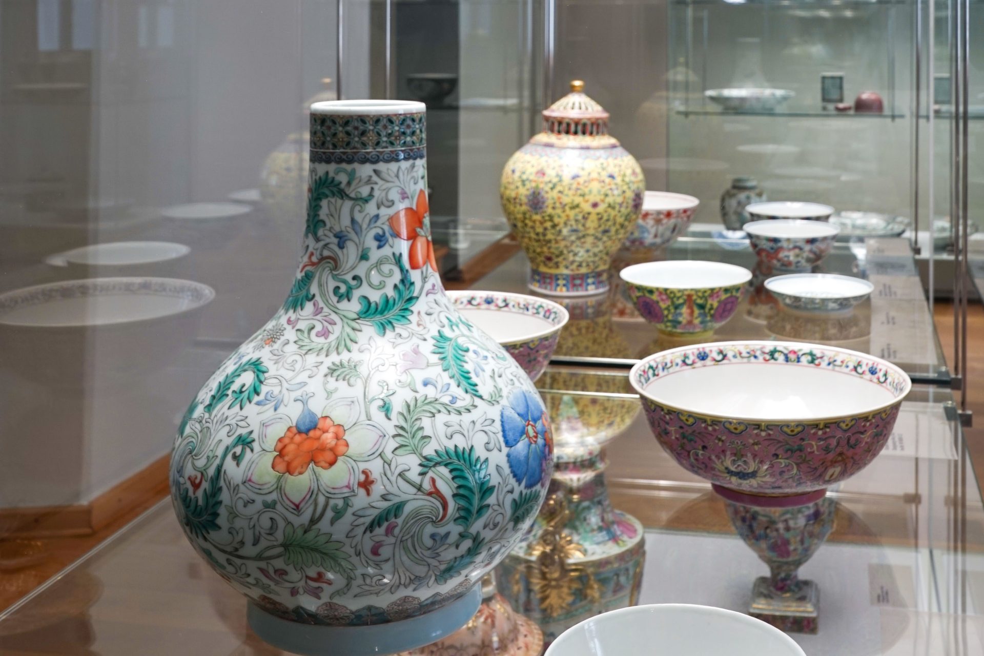 Bunte Keramikwaren und Schalen in einer Museumsausstellung, umgeben von Glas und Holz.