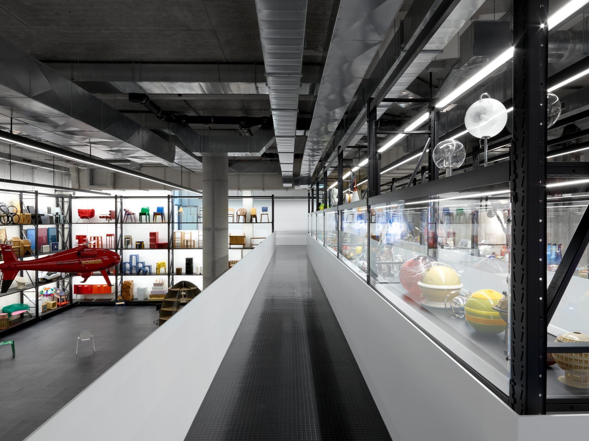Modernes Ausstellungsdesign mit bunten Objekten in Regalen und einem Rundgang in einem hellen, offenen Raum.