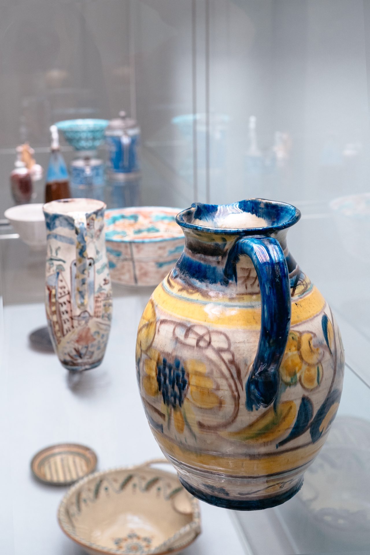Bunt verzierte Keramiken in einer Vitrine, darunter ein großer Krug mit floralen Mustern und diverse Schalen.