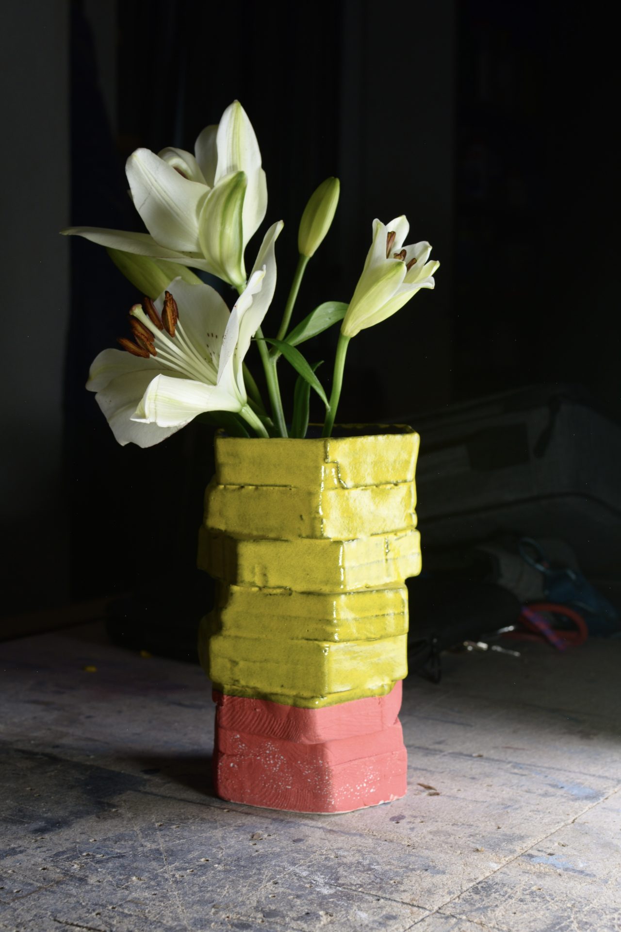 Bunter Behälter mit gelben und roten Teilen. Er ist voll mit weißen Lilienblumen.